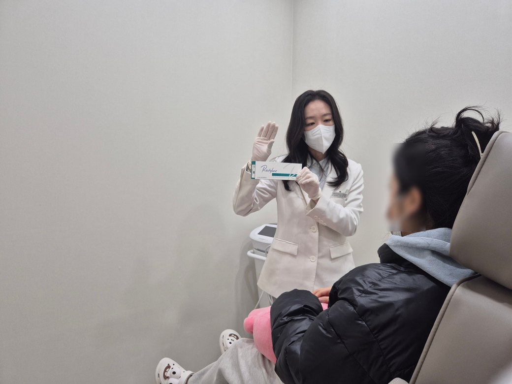 시술 의자에 앉은 환자에게 필러 제품을 보여주며 설명하는 최진숙 원장